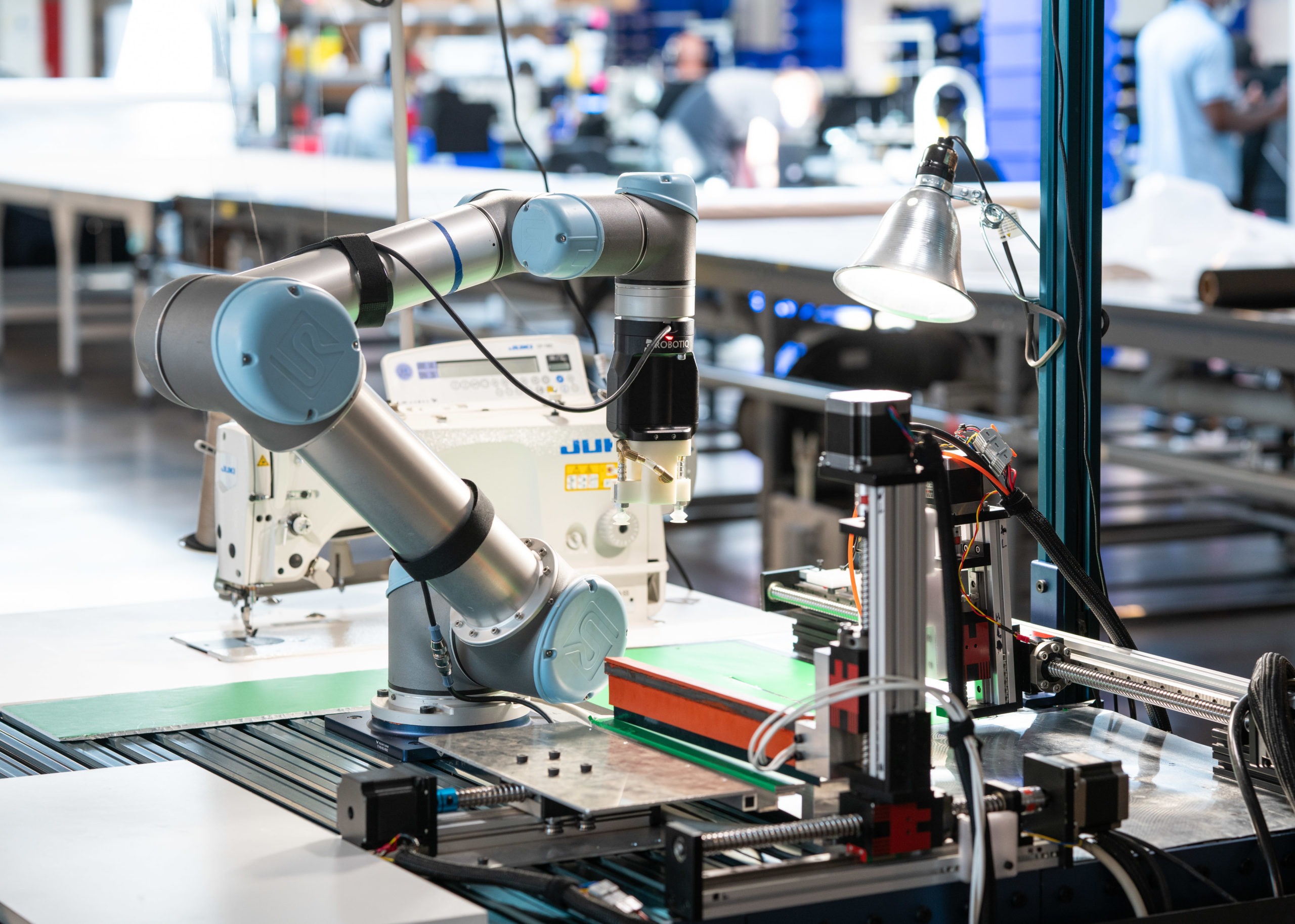 collaborative industrial robot positioned in front of a sewing machine with other automated tools adjacent